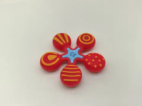 Five-petal silicone part in red and yellow with a light blue centre, each petal carrying a different moulded pattern.